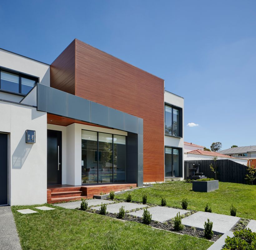 Flaches, modernes Wohnhaus mit klaren Linien, Holzverkleidung und gepflegtem Vorgarten bei Sonnenschein.