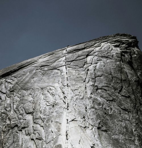 Steil aufragende Felswand mit rauer, heller Oberfläche und senkrechtem Riss unter dunklem Himmel.